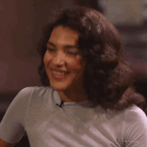Woman With Curly Hair In Light Blue Shirt Smiling GIF