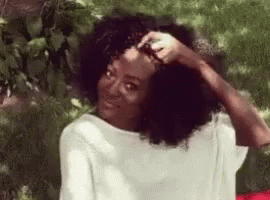 Woman With Curly Hair Sitting in Grass Hand on Head