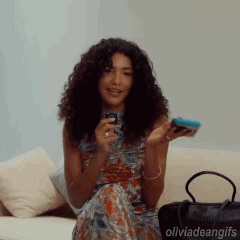 Woman With Curly Hair Sitting On Couch Holding Cell Phone GIF