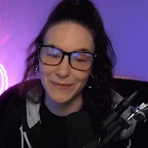 Woman With Glasses and Black Shirt Smiling in Front of Microphone