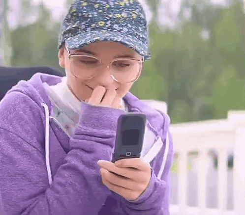 Woman With Glasses and Hat Holding Flip Phone
