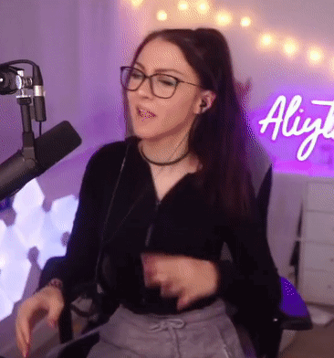 Woman With Glasses Sitting at Microphone in Front of Aliyja Sign