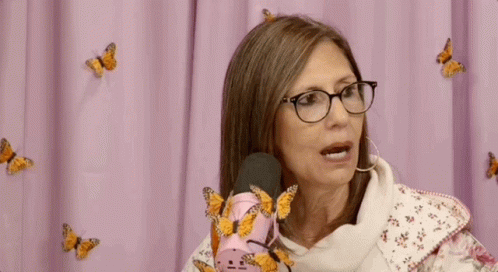 Woman With Glasses Sitting At Pink Microphone With Butterflies GIF