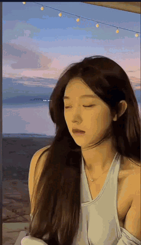Woman With Long Hair Standing in Front of Water Eyes Closed White Tank Top