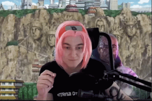 Woman With Pink Hair Sitting at Microphone in Black TRNA Shirt