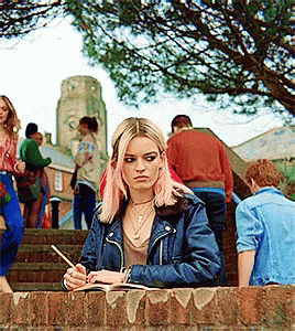 Woman With Pink Hair Writing In Notebook On Brick Wall GIF