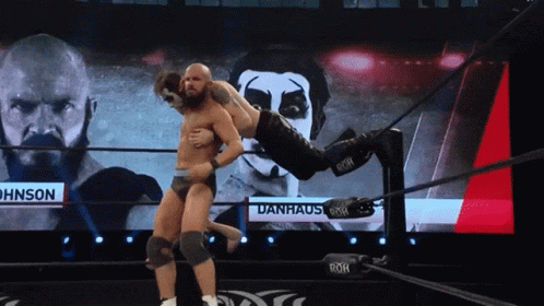 Wrestler Lifted by Another Wrestler in Front of Danhaus Screen
