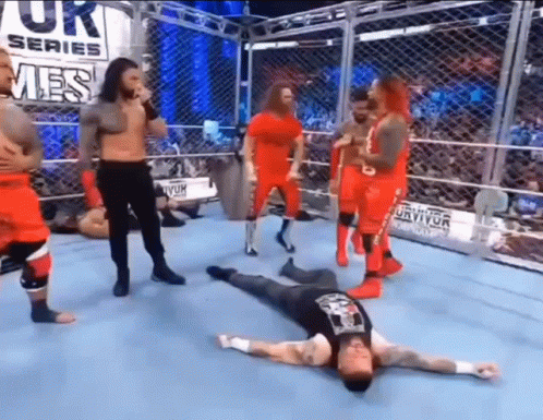 Wrestlers Standing Around Man Laying on Floor