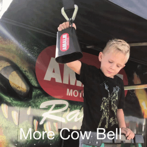 Young Boy Holding Cow Bell in Front of More Cow Bell Sign
