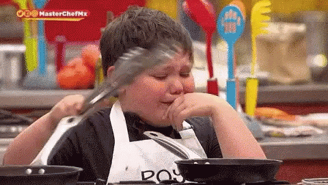Young Boy in Apron Holding Tongs Over Mouth While Cooking