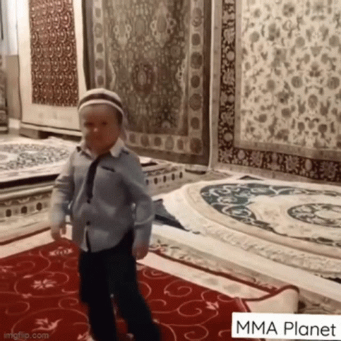 Young Boy In Blue Shirt And Tie Standing On Rug GIF