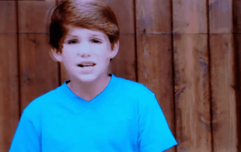 Young Boy in Blue Shirt by Wooden Fence