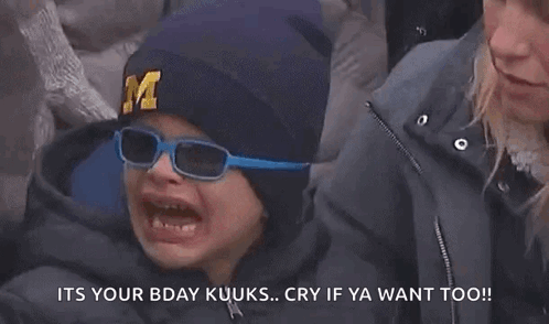 Young Boy in Hat With Letter M Crying While Woman Looks On