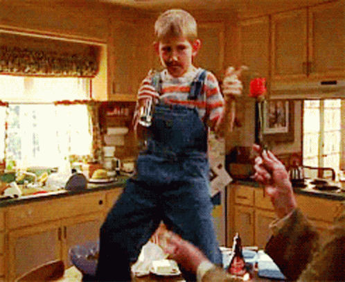 Young Boy in Overalls Standing on Table Holding Glass