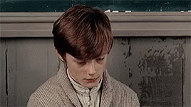 Young Boy in Sweater Sitting in Front of Chalkboard