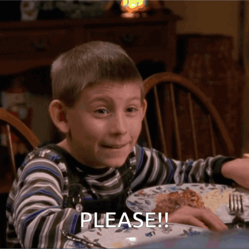 Young Boy Sitting at Table With Plate of Food Saying Please