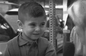 Young Boy Standing Next to Shelf Black and White