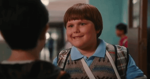 Young Boy With Backpack Talking to Another Boy in School Hallway
