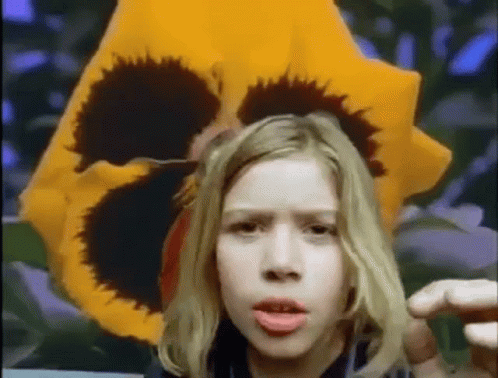 Young Girl Before Yellow Flower With Black Center GIF
