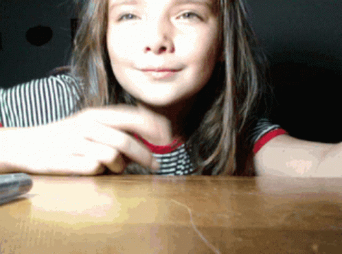 Young Girl Sitting at Table With Remote Control