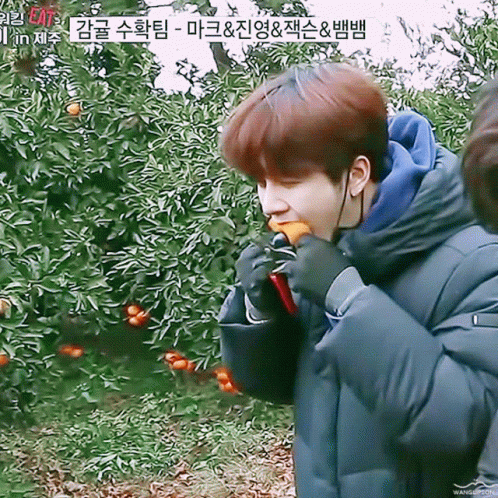 Young Man Eating Orange in Front of Tree With Chinese Writing