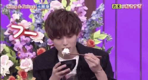 Young Man Eating Rice and Using Phone Beside Flowers