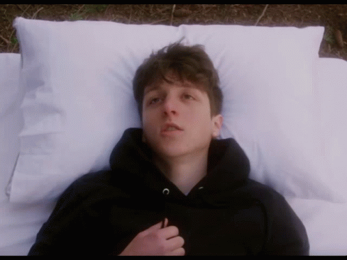 Young Man in Black Hoodie Laying on Bed with White Pillows