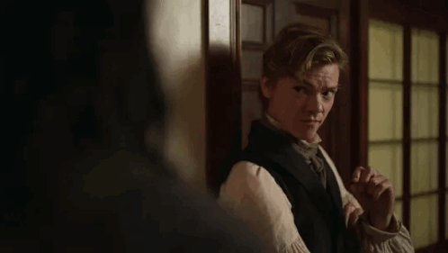 Young Man In Black Vest And Tie By Door In Dark Room GIF