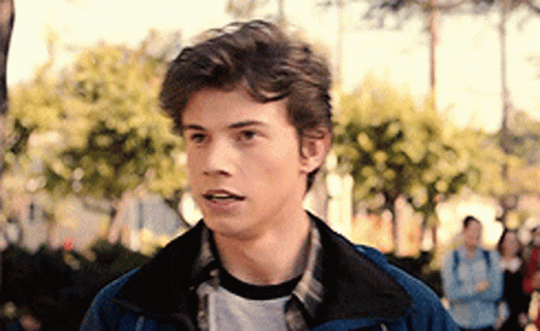 Young Man in Blue Jacket and Plaid Shirt Standing by Trees