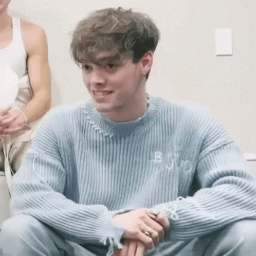 Young Man in Blue Sweater Smiling with Folded Hands