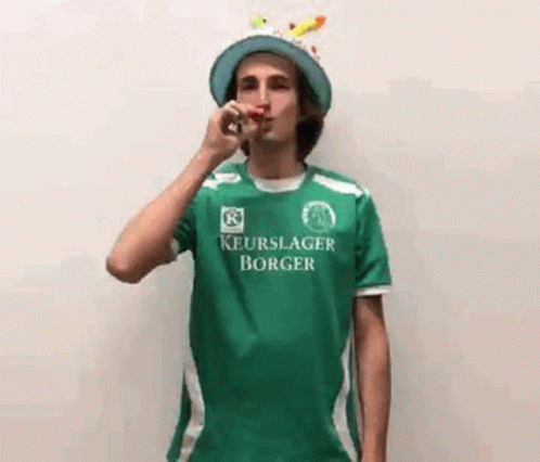 Young Man In Green Shirt Blowing Party Horn GIF