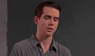Young Man In Grey Shirt Against Black Wall GIF