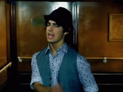 Young Man In Hat And Vest Standing In Elevator GIF