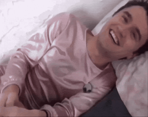 Young Man in Pink Shirt Laying on Bed Smiling