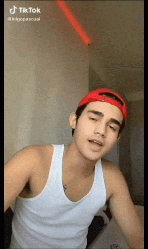 Young Man In Red Hat And White Tank Top Making TikTok Video GIF