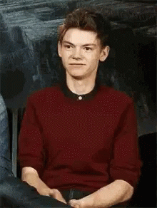 Young Man In Red Sweater Sitting With Hands Folded GIF