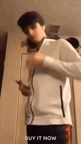 Young Man in White Jacket Holding Cell Phone By Door