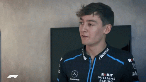 Young Man in Williams Racing Jacket Standing Before TV