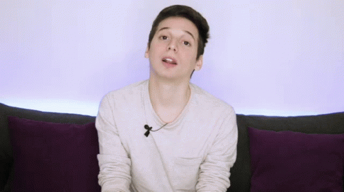 Young Man on Couch With Purple Pillows Gesturing