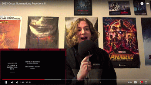 Young Man Speaking Into Microphone In Front Of Avengers And Inception Posters GIF