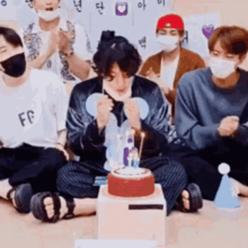 Young Men in Face Masks Sitting Around Cake