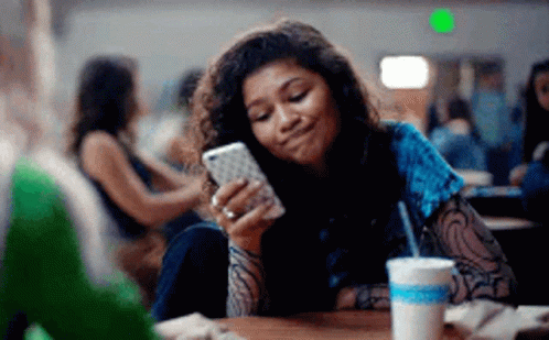 Young Woman Sitting At Table Looking At Cell Phone GIF
