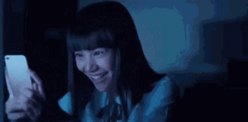 Young Woman Smiling at Phone in Dark