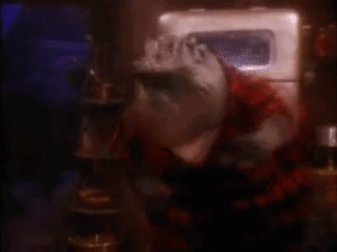 A Baby Dinosaur Is Laying On The Ground With Its Arms Outstretched In A Dark Room . GIF