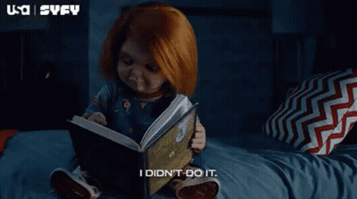 A Baby Doll Is Sitting On A Bed Reading A Book . GIF