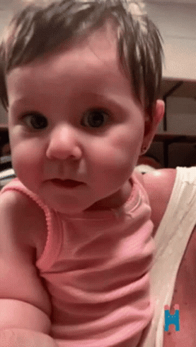 A Baby Girl In A Pink Tank Top Is Being Held By A Woman GIF