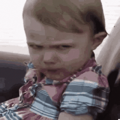 A Baby Girl Is Making A Funny Face While Sitting On A Couch . GIF