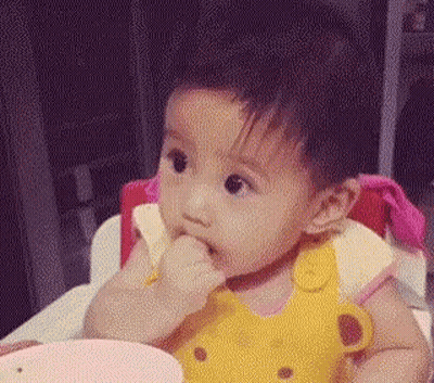 A Baby Girl Is Sitting In A High Chair Eating Food From A Bowl . GIF