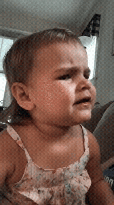 A Baby Girl Is Sitting On A Couch And Crying . GIF