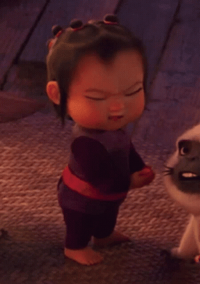 A Baby Girl Is Standing Next To A Cat And Making A Funny Face . GIF